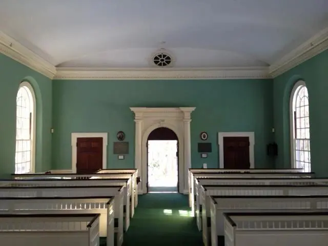 A church with pews and green carpet in front of the door.